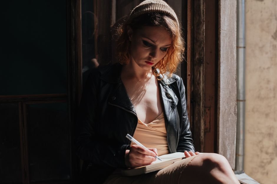 A woman writing in a journal by a window
